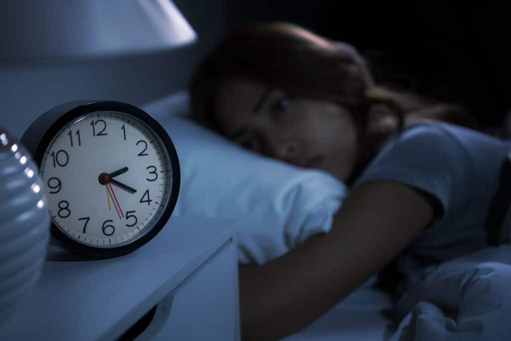 Frau mit Schlafstörung und schaut auf ihren Wecker