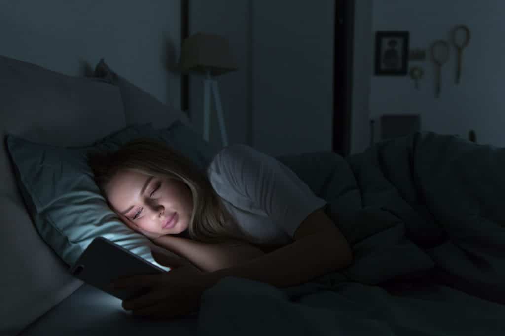 Frau mit Schlafstörung ist am Handy und kann nicht schlafen
